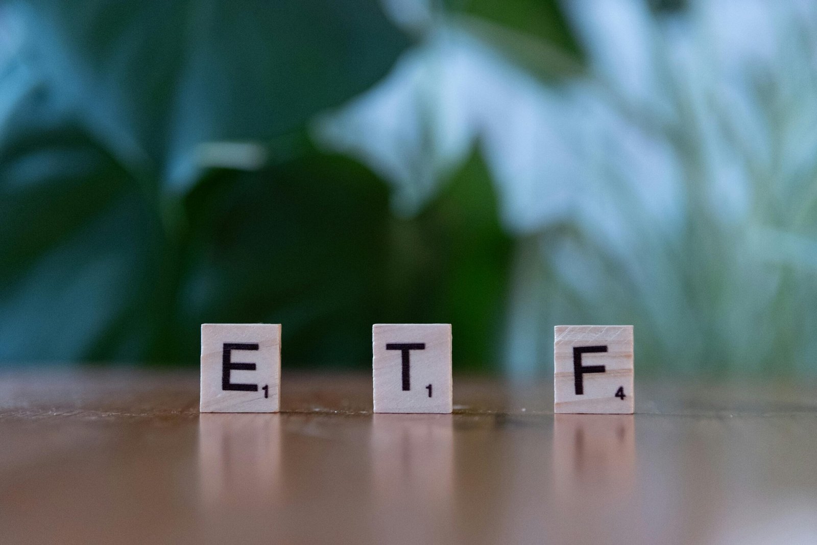 Scrabble tiles spelling ETF on a wooden surface with blurred green background.